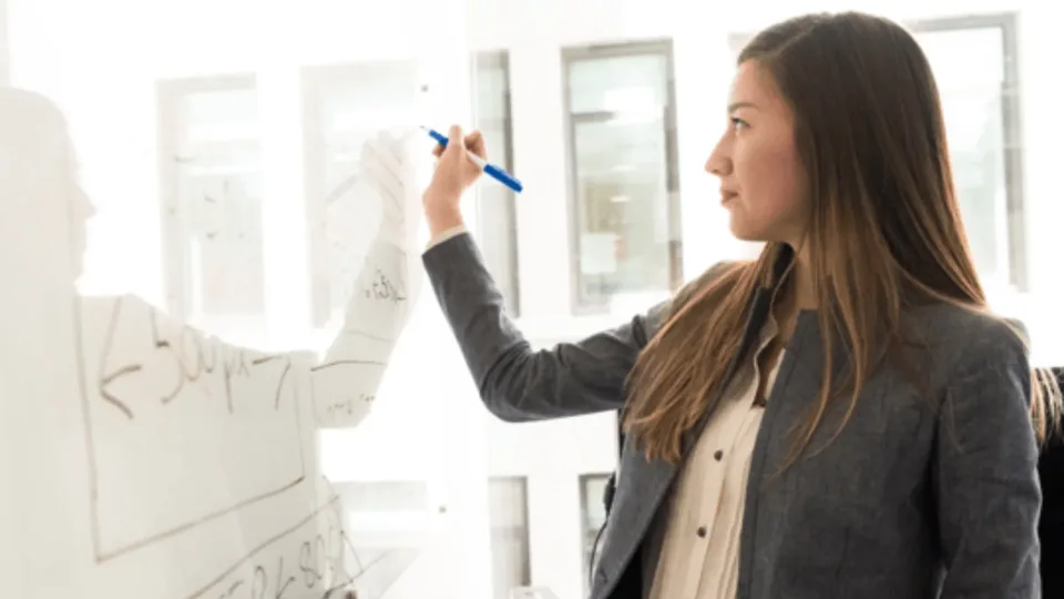 Woman adding notes to a whiteboard during a planning session.