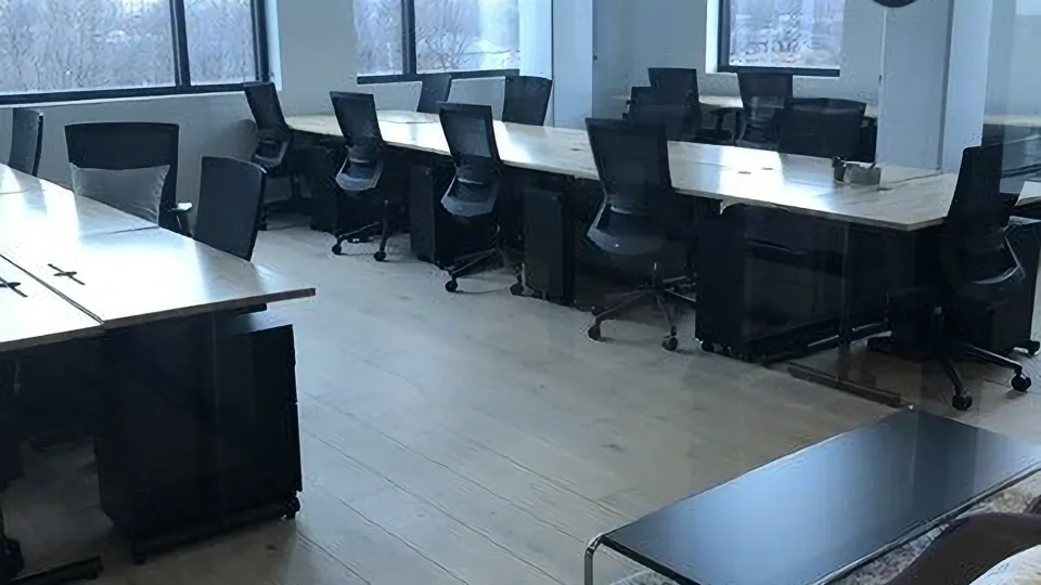 Office workstations with monitors and chairs beside large windows.