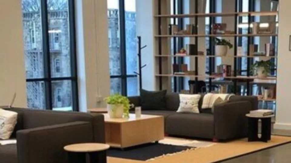 Open office lounge with seating, shelving and large windows.